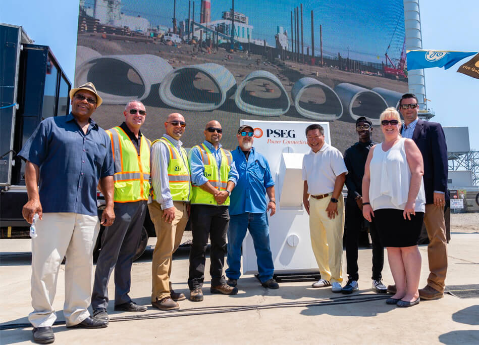 A diverse group of United Rentals employees stand together at a construction site.