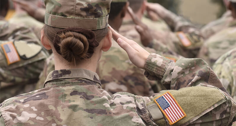 Soldiers in fatigues stand at attention facing away from the camera and saluting.